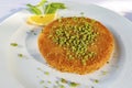 Traditional turkish kunefe dessert with grated pistachios, sliced lemon and mint on plate.