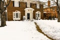 Traditional two story brick house with bay windows and pillared porch in the snow with the sidewalk cleared