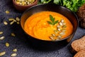 Traditional Ukrainian autumn cream soup of pumpkins and carrots with seeds and parsley on a dark background