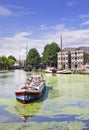 Traditional vessel in canal with green algae and a monumental mansion, Gouda, Netherlands