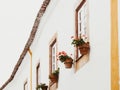 Traditional white and yellow stone house with tiled roof and hanging clay pots with blooming geraniums