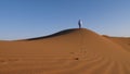 A traditionally dressed Moroccan man wearing a blue gandoura, djellaba and a turban walks on a sand dune, Erg Chegaga desert, Moro