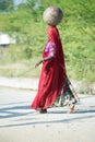 Traditionally dressed woman in traditional indian Saree walking at rural road with pot at head. Rajasthan. India