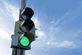 Traffic light in green color, with a blue sky and cloud in the background.