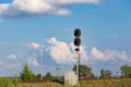 Traffic light on the railway in the village against the background of the forest and blue sky with white clouds on a bright sunny Royalty Free Stock Photo