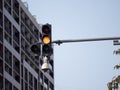 A traffic light with a yellow light is on a street in front of a building. A CCTV security camera is mounted on the Royalty Free Stock Photo