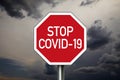 Traffic sign with dark cloudy sky with message Stop Covid 19