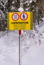 Yellow black warning sign and signs in German, English, Italian and French: Closed, Danger of avalanche. Snow-covered forest Royalty Free Stock Photo