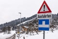 Red triangle road traffic warning sign - Other Danger with text Ausfahrten which means Exits. Snow covered road, trees and mountai