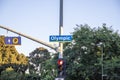 A traffic signal with a red light and a street sign that reads Olympic surrounded by lush green trees with a clear blue sky Royalty Free Stock Photo