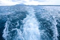 Trail and foamy waves on blue sea surface behind of moving boat with island background Royalty Free Stock Photo