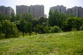 Trail in grass on ridge of slopes before apartments in trees of