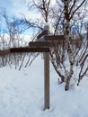 Trail marking post in snowy landscape on the polar circle. Solid wooden post with arrows indicating paths in the middle of the