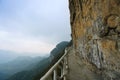 The trail on the mountain wall is surrounded by clouds and mist in the distance.