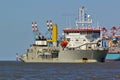 Trailing suction hopper dredger in the Weser estuary with container vessel and port facilities in the background