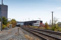 Train coming down a track running alongside industrial buildings in a rural area, fall season with autumn leaves Royalty Free Stock Photo