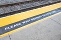 Train platform with sign please wait behind the yellow line and yellow marked warning area Royalty Free Stock Photo