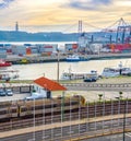 Train on railroad by comercial port with ships and containers, 25 de Abril Bridge over Tagus river at sunset, Christ the King