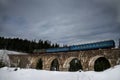 The train rides on an old stone bridge viaduct in the coniferous forest. Winter landscape. Ukraine. Vorokhta. Royalty Free Stock Photo