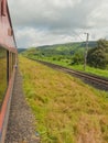 Red coloured train running through the mountain ranges of Sahyadri with mountains and cloudy sky in the background. Royalty Free Stock Photo