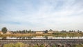 Train tracks beside a lake with a hill of land and trees with green foliage on a barren terrain in the background Royalty Free Stock Photo