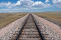 Train Tracks on an Open Plain Stretching Out to a Blue Sky and Clouds on the Horizon Royalty Free Stock Photo