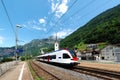 A train travels on the railway curving through a Swiss village with churches on the hillside and majestic Alpine mountains