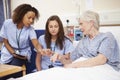 Trainee Nurse Sitting By Female Patient's Bed In Hospital