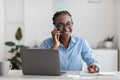 Office Trainee. Black woman talking on cellphone and taking notes at workplace Royalty Free Stock Photo