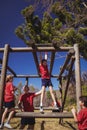 Trainer assisting girl to climb monkey bars during obstacle course training Royalty Free Stock Photo