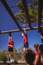 Trainer assisting girl to climb monkey bars during obstacle course training Royalty Free Stock Photo