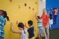 Trainer assisting kids in climbing wall Royalty Free Stock Photo