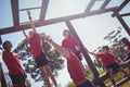 Trainer assisting kids to climb monkey bars during obstacle course training Royalty Free Stock Photo