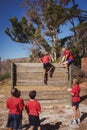 Trainer assisting kids to climb a wooden wall during obstacle course training Royalty Free Stock Photo