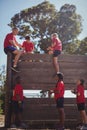 Trainer assisting kids to climb a wooden wall during obstacle course training Royalty Free Stock Photo