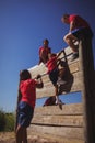 Trainer assisting kids to climb a wooden wall during obstacle course training Royalty Free Stock Photo