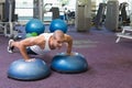 Male in late 20s doing push-ups on blue BOSU-style trainers at gym wearing white tank top Royalty Free Stock Photo