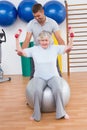 Trainer helping senior woman lift dumbbells on exercise ball Royalty Free Stock Photo