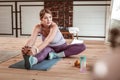 Attentive woman sitting on her old yoga mat and warming up