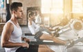 Training, man and rowing machine in gym for group class, fitness workout and cardio exercise. Strong bodybuilder Royalty Free Stock Photo