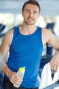 Training to keep toned. A happy man leaning on a treadmill at the gym holding a water bottle. Royalty Free Stock Photo