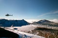 Tramping rescue helicopter in wild mountains snowy landscape with deep blue lake above the clouds, rescuing trampers, New Zealand