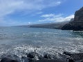 Tranquil beach scene with a rocky shoreline with waves crashing against them in Tenerife