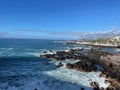 Tranquil beach scene with a rocky shoreline with waves crashing against them in Tenerife