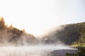 Tranquil bright early morning landscape with mist on lake - soft haze on water and lush green forest in golden sunbeams Royalty Free Stock Photo