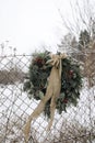 Tranquil december outdoor scene. Christmas advent wreath with beige silk tied bow on old fence. Snow covered landscape