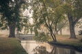 Tranquil deserted autumn foggy morning in a city park. pedestrian bridge through a narrow shallow rivulet with reflection of Royalty Free Stock Photo