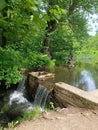 Small Waterfall Over Stone Dam in Forest Park with Pond and Statue Royalty Free Stock Photo