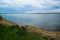 Tranquil lake view. Folding fisherman chair at the coast. Blue cloudy rainy sky