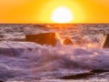 a wave in the ocean on the rocks with a sun setting Royalty Free Stock Photo